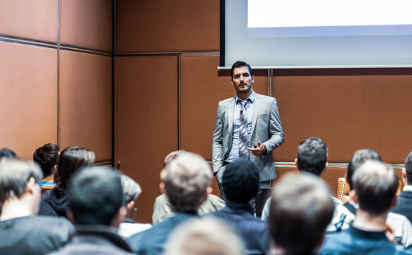 Speaker giving a talk in conference hall at business meeting event. Rear view of unrecognizable people in audience at the conference hall. Business and entrepreneurship concept.