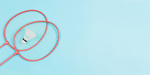 Two badminton rackets on colored background and a badminton ball in between. Lay top view shot with copy space.