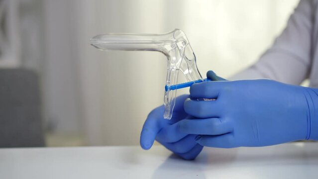 Close-up hands of gynecologist in gloves holding cusco vaginal speculum. Unrecognizable Caucasian man sitting at table in hospital with gynecological instrument