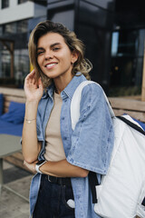 Pretty young caucasian woman smiles teeth at camera walking around city during day. Blonde wears...
