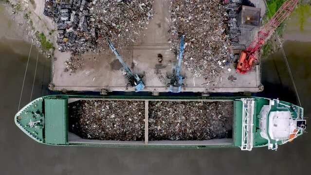 Cranes working simultaneously to load cargo ship with scrap metal at a tidal river port 4K