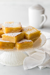 Homemade sweet lemon squares on a pedestal stand sprinkled with powdered sugar.
