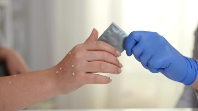 Doctor passing condom to ill young woman with monkey pox rash in slow motion. Unrecognizable Caucasian physician giving sex protection to sick lady in hospital