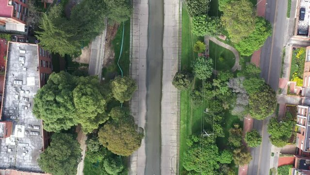 View from a drone of a water canal that is located between a park with trees, a pedestrian bridge and a children's playground in a residential neighborhood of the city of Bogot&aacute;, Colombia.
