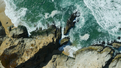 Top down aerial of emerald ocean water and stone cliffs near San Francisco, California
