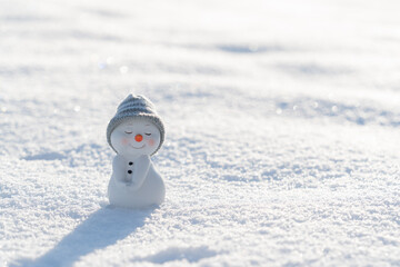 Figure of little cute snowman in a knitted hat and scarf on on snowy field in a sunny winter day....