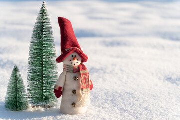 Figure of little cute snowman in a knitted hat and scarf on on snowy field in a sunny winter day. Concept for winter site head mockupcard or christmas card.