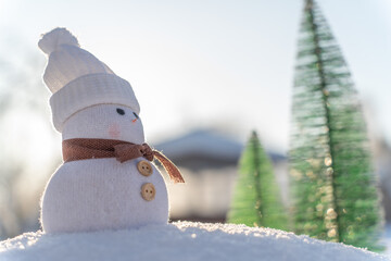 Figure of little cute snowman in a knitted hat and scarf on on snowy field in a sunny winter day. Concept for winter site head mockupcard or christmas card.