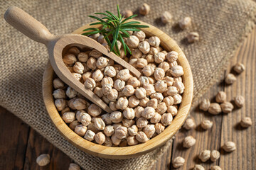 Dried raw chickpeas in wooden spoon and in wooden bowl, on a sackcloth background, closeup. Organic food. Legumes. Top view food. 