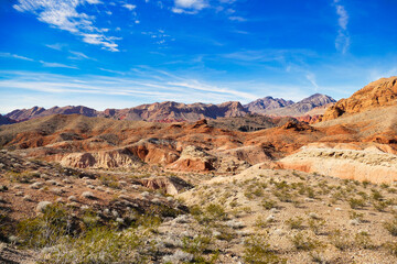 Arid desert landscape with eroded red rocks, sparse vegetation and dark mountains in the background, in Valley of Fire State Park, Nevada, USA.
