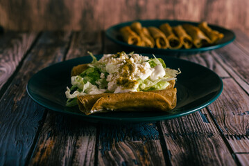 Tacos flauta with cheese, cream and lettuce on a wooden table. Mexican snacks.