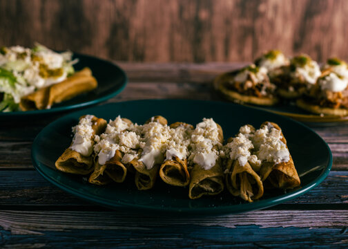 Tacos flauta with cheese and cream on a wooden table. Mexican snacks.