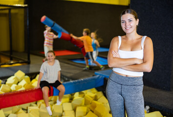 Cheerful young girl in sportswear standing indoors near foam pit with battle beam on background of...