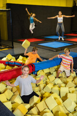 Group of excited active children having fun while playing and jumping in soft cubes in the dry pool...