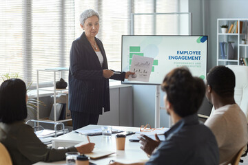 Portrait of senior businesswoman giving presentation in office while leading meeting with team, copy space