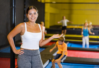 Positive woman trampolining coach against the background of children playing and jumping on a trampoline