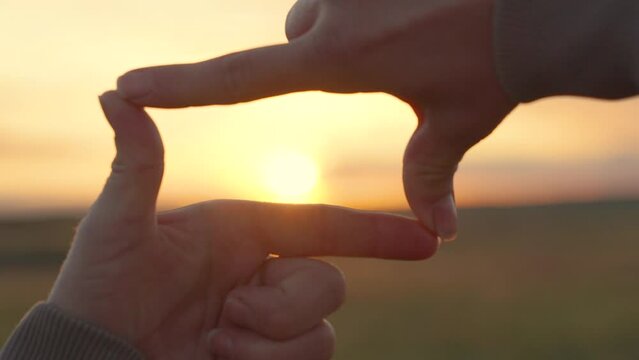 Hands of young female director cameraman making frame gesture at sunset in park. Sees like in movies. Concept of seeing world as different. Business planning. Girl shows her fingers frame symbol, sun