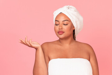 Pretty oversize black lady covered in towel holding something invisible on her palm, recommending...