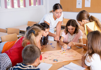 Happy kids and female teacher playing together educational board game in classroom at school
