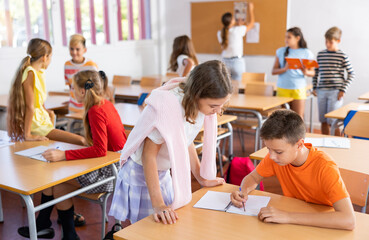 Young girls and boys performing tasks in school together, writing in copybook.