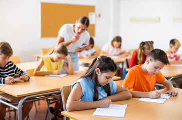 Fototapeta premium Young girl and boy studying subject in classroom, listening to teacher and writing.