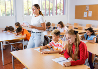 Group of school kids with pens and notebooks studying in classroom with teacher