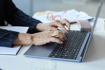 Close up of senior female hands typing at laptop keyboard while working in office, copy space