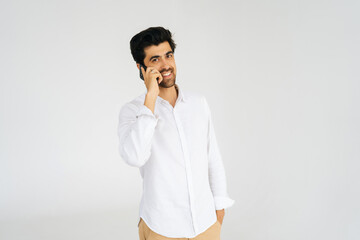 Studio portrait of cheerful young man talking smartphone, having conversation on mobile phone, holding and using cellphone on white isolated background, looking at camera. Communication concept.