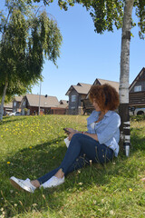 a beautiful young woman sitting in a park looking at her phone