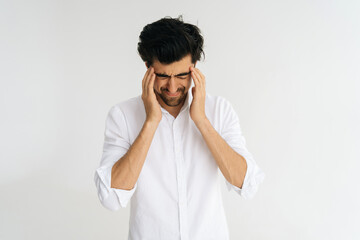 Studio portrait of frustrated young man with closed eyes massaging temples suffering from headache painful, migraine, doubt make complicated decision standing on white isolated background.