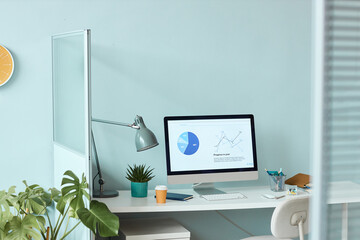 Minimal office workplace with light blue wall and statistics graphs on computer screen, copy space