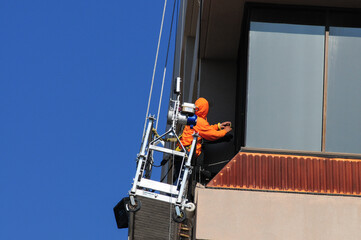 Maintenance worker using a suspended platform prepping exterior walls of a high-rise building prior to painting   