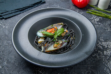 black spaghetti with seafood on black plate on grey table