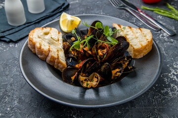 Mussels in wine sauce on black plate on grey table
