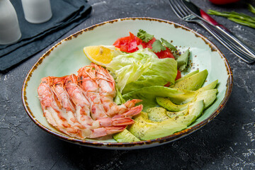 some langoustines on a plate with avocado on grey concrete table