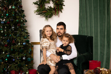 portrait of father and girls sister smile on a background of Christmas trees in the interior of the house