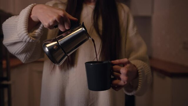 A woman pours coffee into a cup from a coffee maker moka pot. The moka pot is a stove-top or electric coffee maker that brews coffee by passing boiling water pressurized by steam through ground coffee