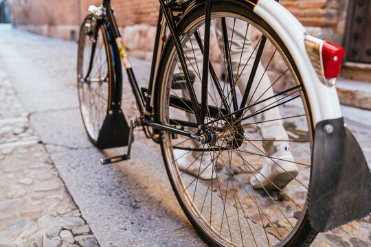Close-up image of man pushing his vintage classic bicycle through city alleys. Seen from behind.