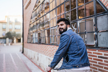 Young man in denim jacket sitting on top of his vintage classic bicycle looking to the side.