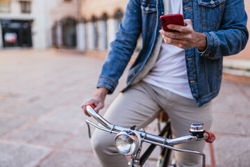 Cropped image of a young man in denim jacket consulting his cell phone on his vintage classic bicycle in the city.