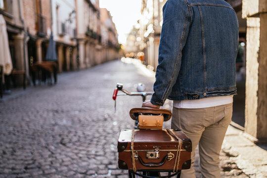 Cropped image of a young man with his back turned, wearing a denim jacket and riding his classic vintage bicycle through the streets of his hometown.