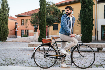Young man in denim jacket standing on top of his vintage classic bicycle looking backwards. Profile...