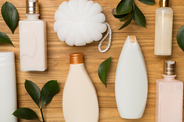 Different cosmetic bottles and washcloth on wooden background, top view