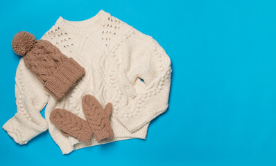 Sweater and winter hat with mittens on color background, top view