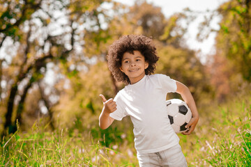 Obraz premium Curly-haired boy in white sportswear with a football