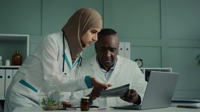 Multiracial doctors colleagues discuss teamwork african man and arabian woman two professional medical workers talk about healthcare check MRI scan use computer app doing online research X-ray results