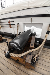 details of an old metal cannon with ropes on in a ship with a wooden floor, assemble old military as a display, nautical tools