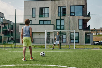 Back view of teenage boy playing football with father standing in gates, copy space