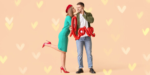 Happy young couple with balloon in shape of word LOVE on beige background