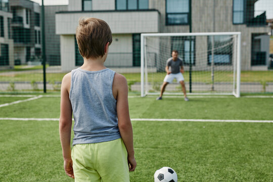 Back view of young boy playing football with father standing in gates and scoring goal, copy space